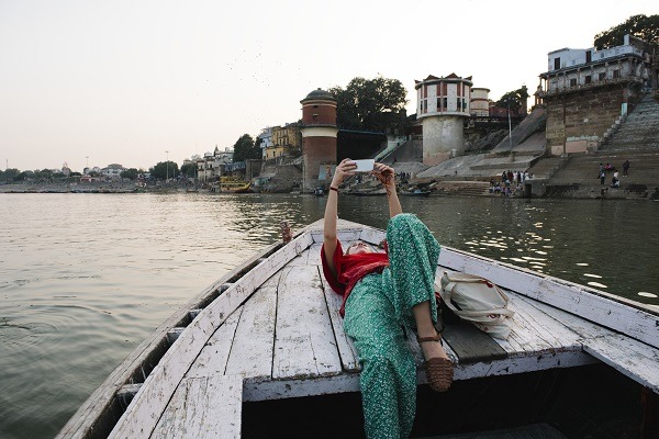 Vestlig kvinne som ligger på en båt og tar selfies i Varanasi
